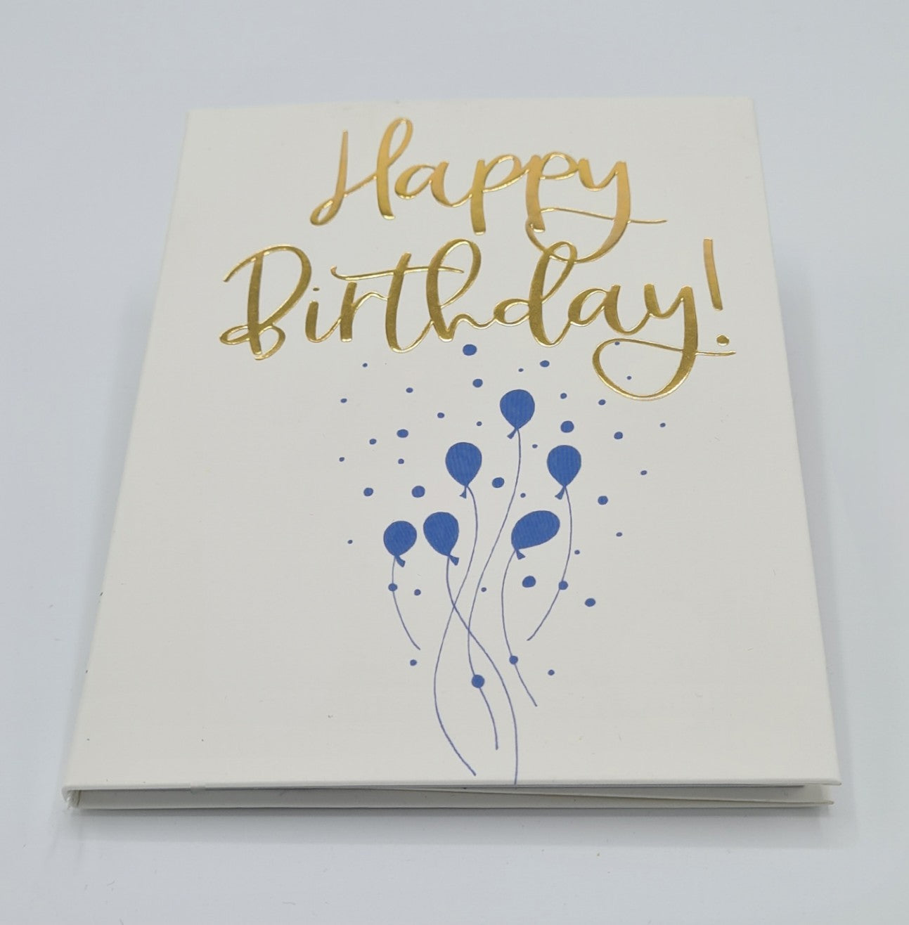 White front cover of little book entitled "Happy Birthday" with the font written in gold. There is an illustration of blue balloons half way down the page.