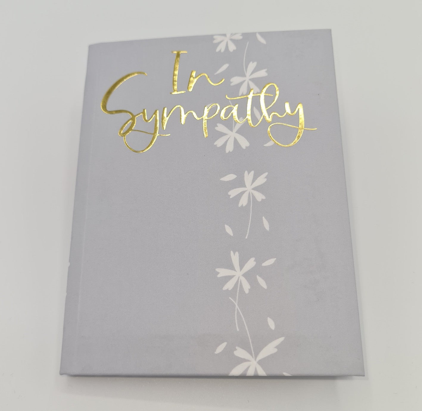 Front cover of little book conveying sympathy for a loss. The cover is grey with the words "In Sympathy" written in gold text and a line of small white flowers drawn from top to bottom of the page.