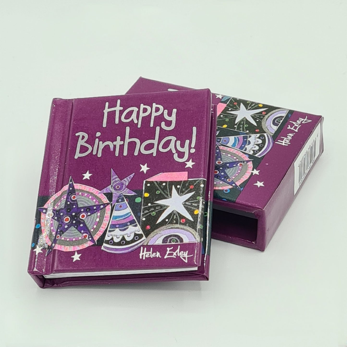 Little purple book entitled "Happy Birthday" with the title written in silver text. The book has its own sleeve and is shown sitting at an angle on top of the sleeve with the sleeve partially visible underneath.