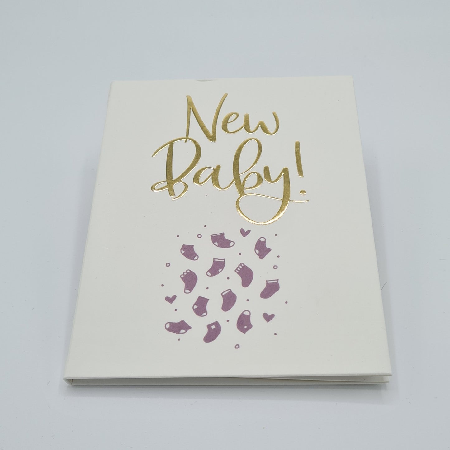 Front cover of little white book with the title "New Baby" written in gold font. There are illustrations of purple baby booties and little hearts on the bottom half of the page.