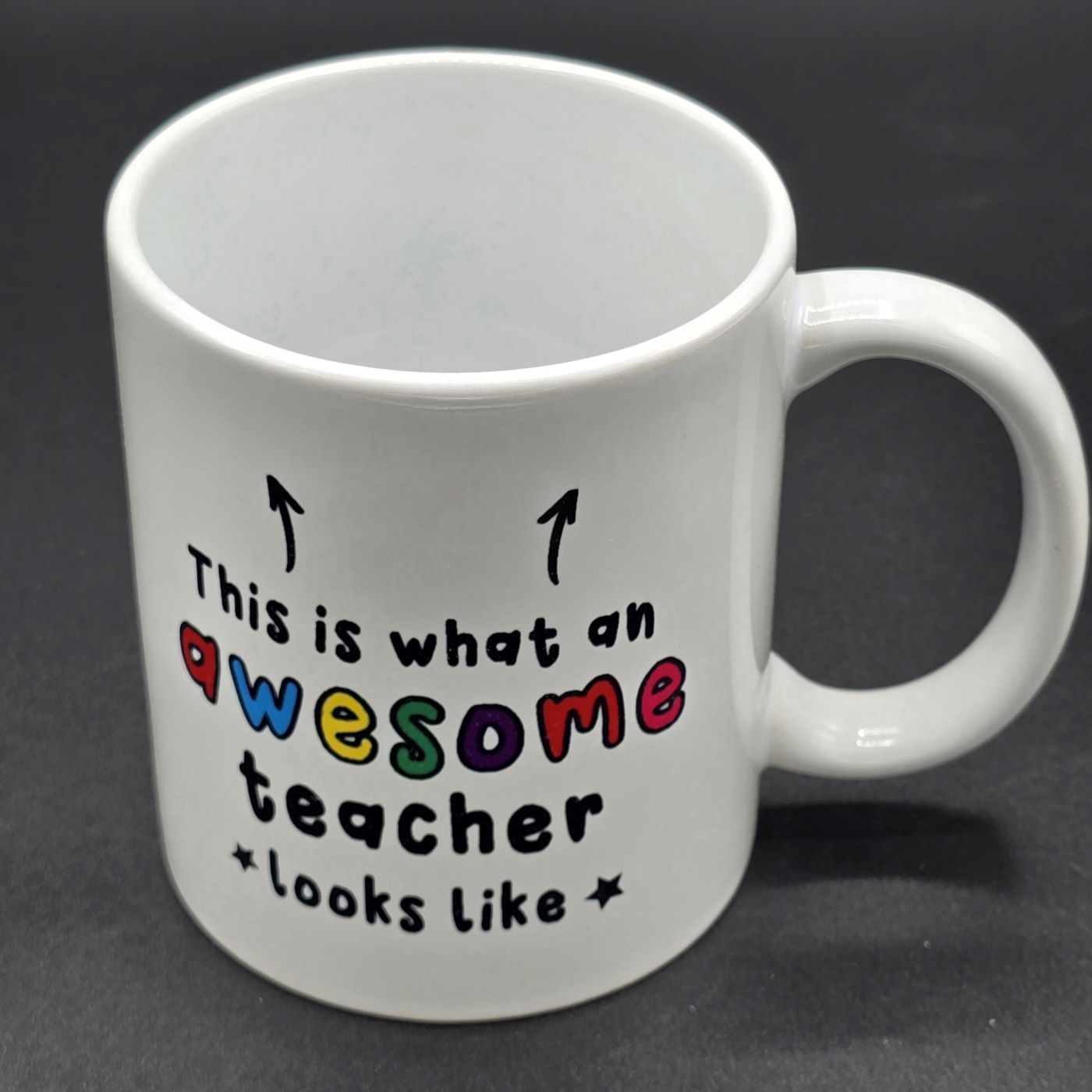 Plain white mug with white handle. Text on mug says "This is what an awesome teacher looks like" with two arrows pointing to the top of the mug.
