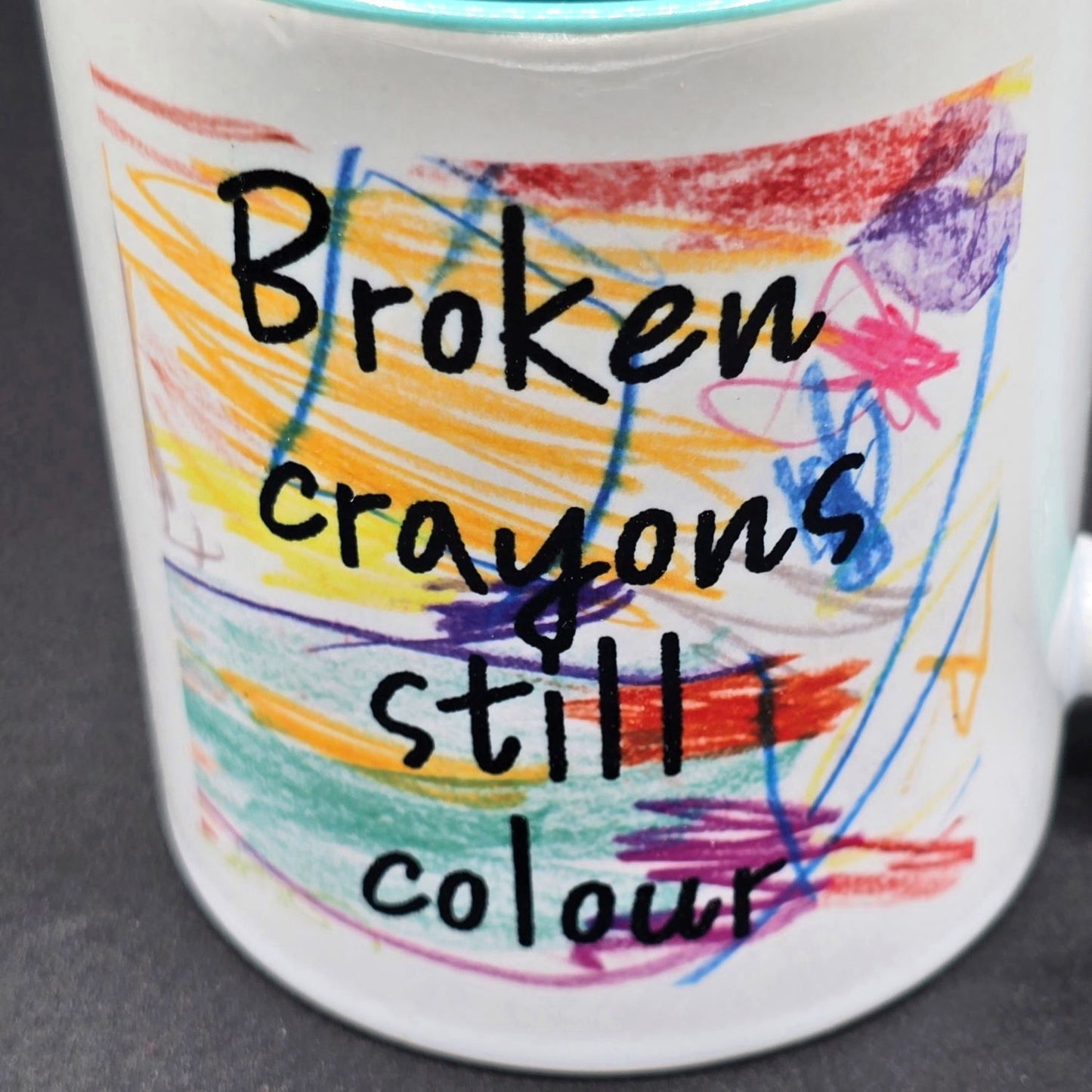 Close up of mug design showing colourful crayon scribbles and the wording "Broken crayons still colour".