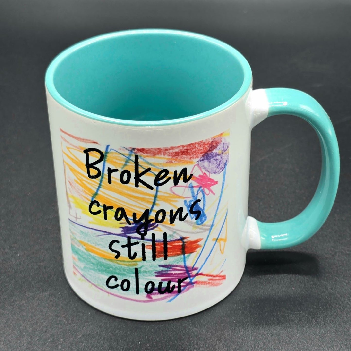 White mug with teal inside and teal handle. Design on mug is colourful crayon scribbles with the wording "Broken crayons still colour".