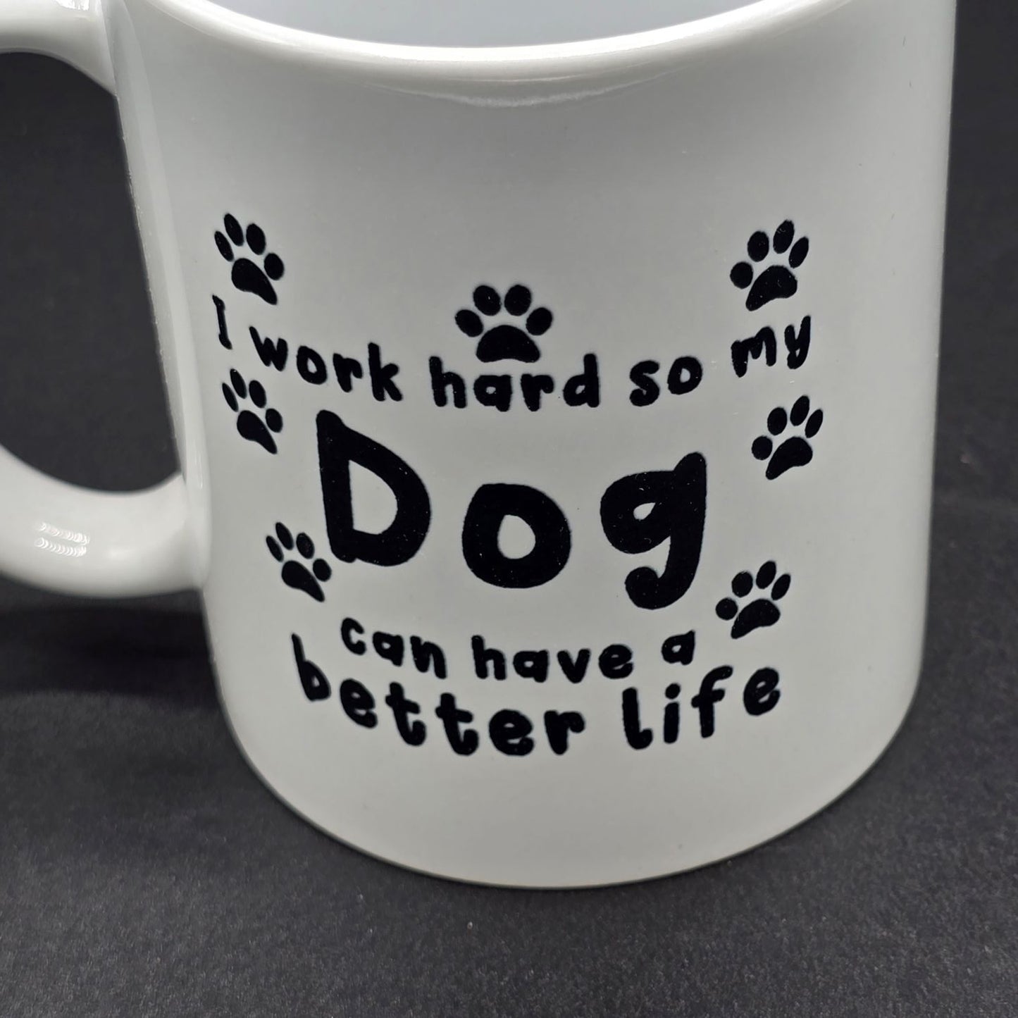 Close up of white mug with the text "I work hard so my dog can have a better life". The text is surrounded by several black paw prints.