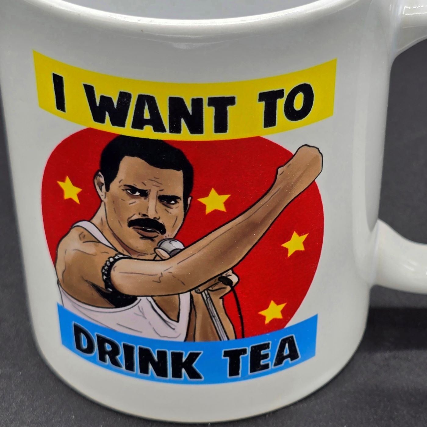 Close up of white mug featuring illustration of Freddie Mercury holding microphone and the slogan "I want to Drink Tea".