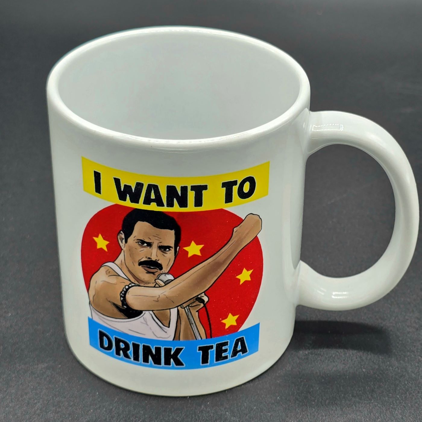 White mug with handle. Design on mug features illustration of Freddie Mercury holding microphone and the slogan "I want to Drink Tea".