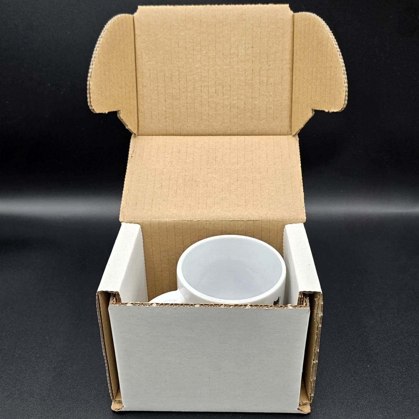 White cardboard box with lid lifted showing top of mug inside.