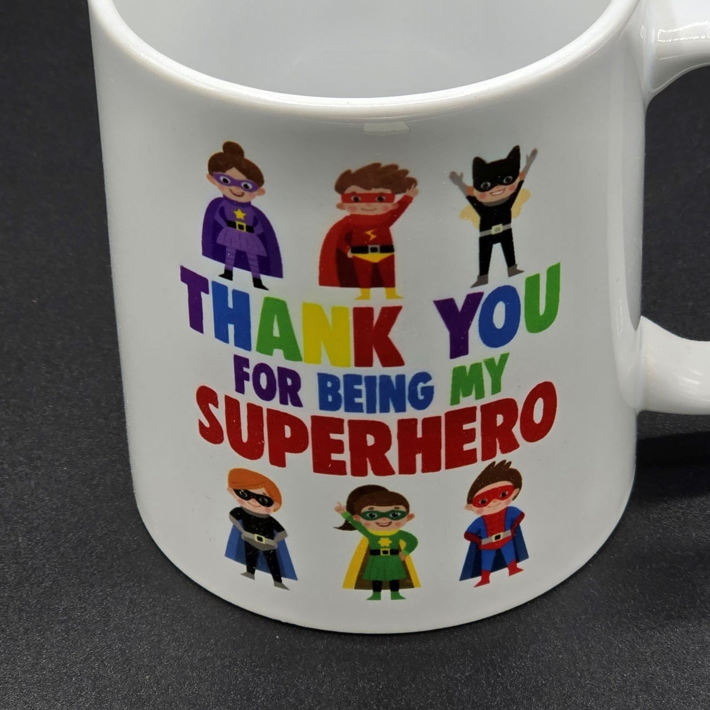 Close up image of white mug with illustrations of six superheroes and the wording "Thank You for Being my Superhero".
