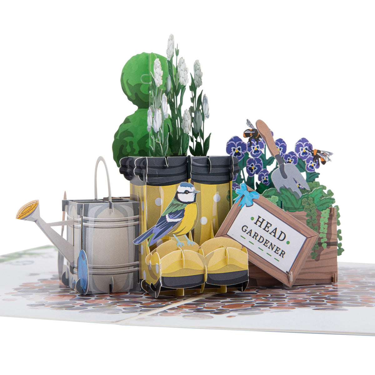 Close up of Spring Wellingtons pop up card showing a pop up pair of yellow wellington boots with a black band at the top of the boots. The boots are surrounded by a silver watering can and a plant pot with purple flowers, foliage and a trowel inside. There is a bluetit bird sitting on one of the wellington boots.
