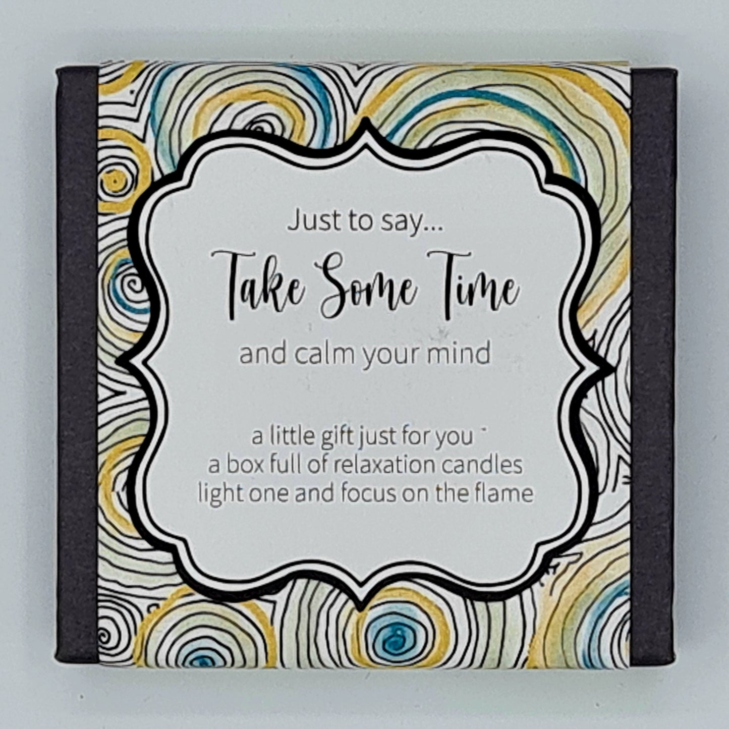 Small black square box with a label with yellow and blue swirls and a white textbox saying "Just to say...Take Some Time and calm your mind. A little gift just for you, a box full of relaxation candles, light one and focus on the flame".