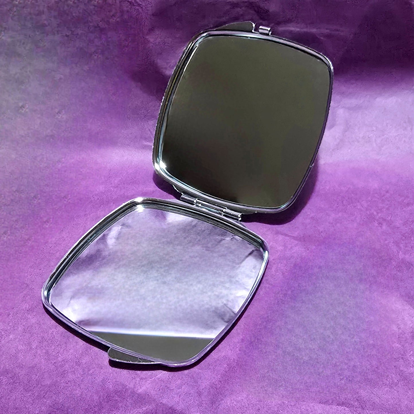 Square silver compact mirror opened up to show the two mirrors on the inside, one on top and one on the bottom.