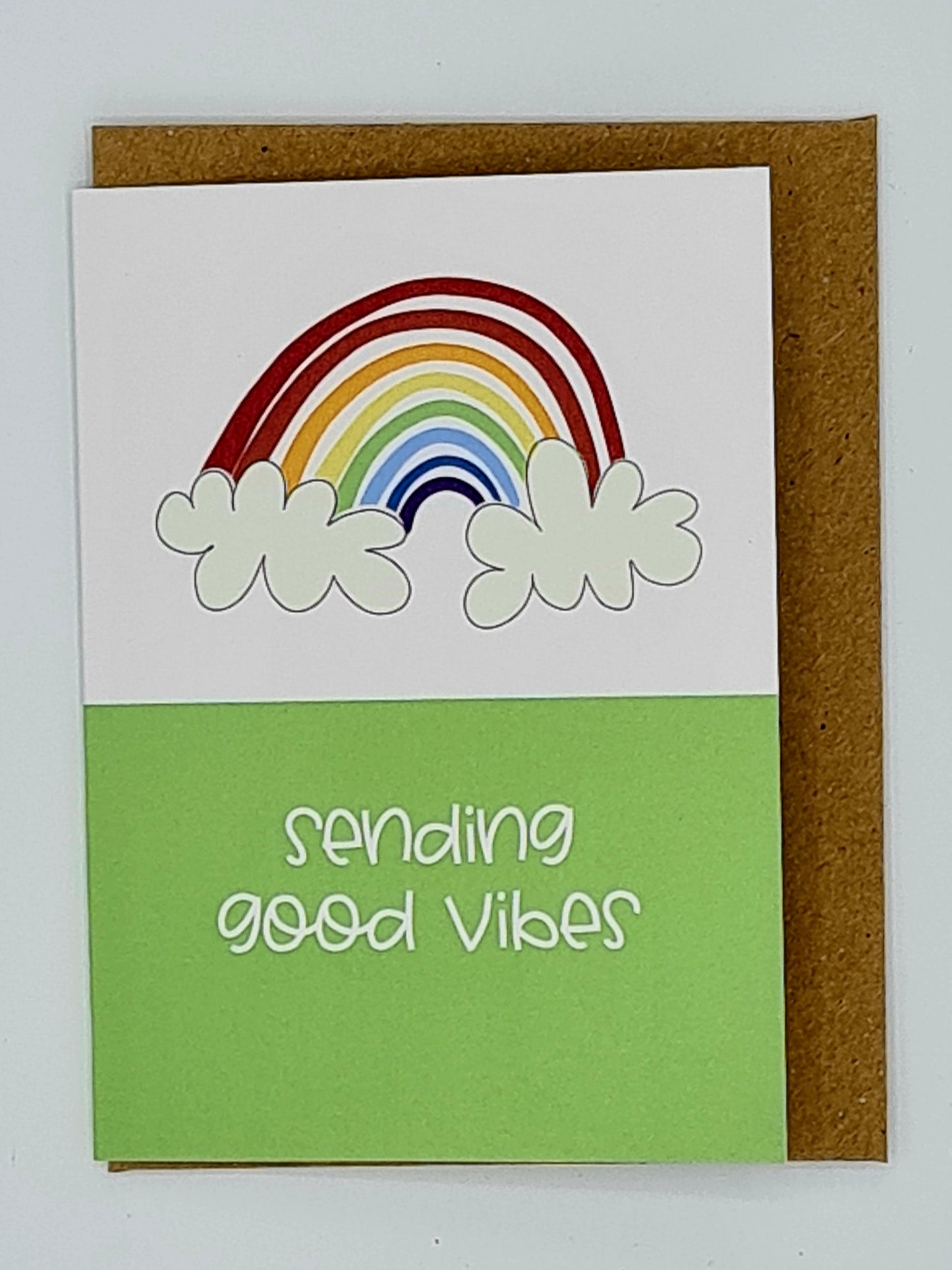A7 mini card with brown envelope. The top half of the card is white with a drawing of a rainbow and clouds whilst the bottom half of the card is green and features the words "sending good vibes" written in white.