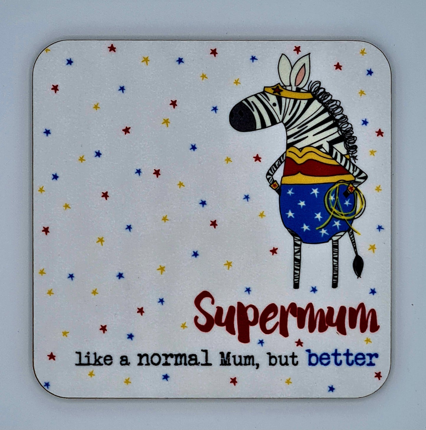 White coaster covered with red, yellow and blue stars. There is a drawing of a zebra dressed as wonder woman and the slogan reads "Supermum, like a normal mum, but better".