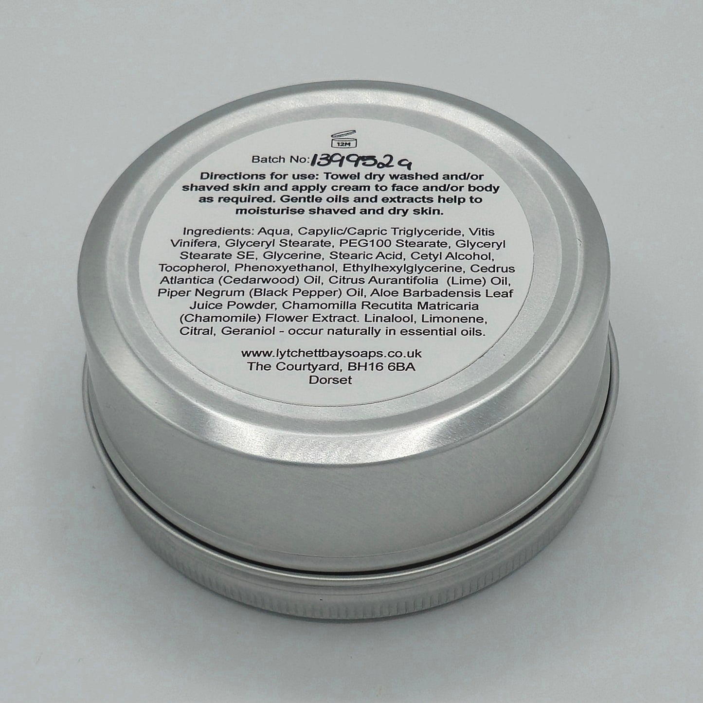 The back or bottom side of the silver tin containing Aftershave, Face & Body Cream for Men by Lytchett Bay Soaps. At the top of the label is that batch no, then bold text saying "Directions for use: Towel dry washed and/or shaved skin and apply cream to face and/or body as required. Gentle oils and extracts help to moisturise shaved and dry skin".
Half down the label there is text containing the ingredients.