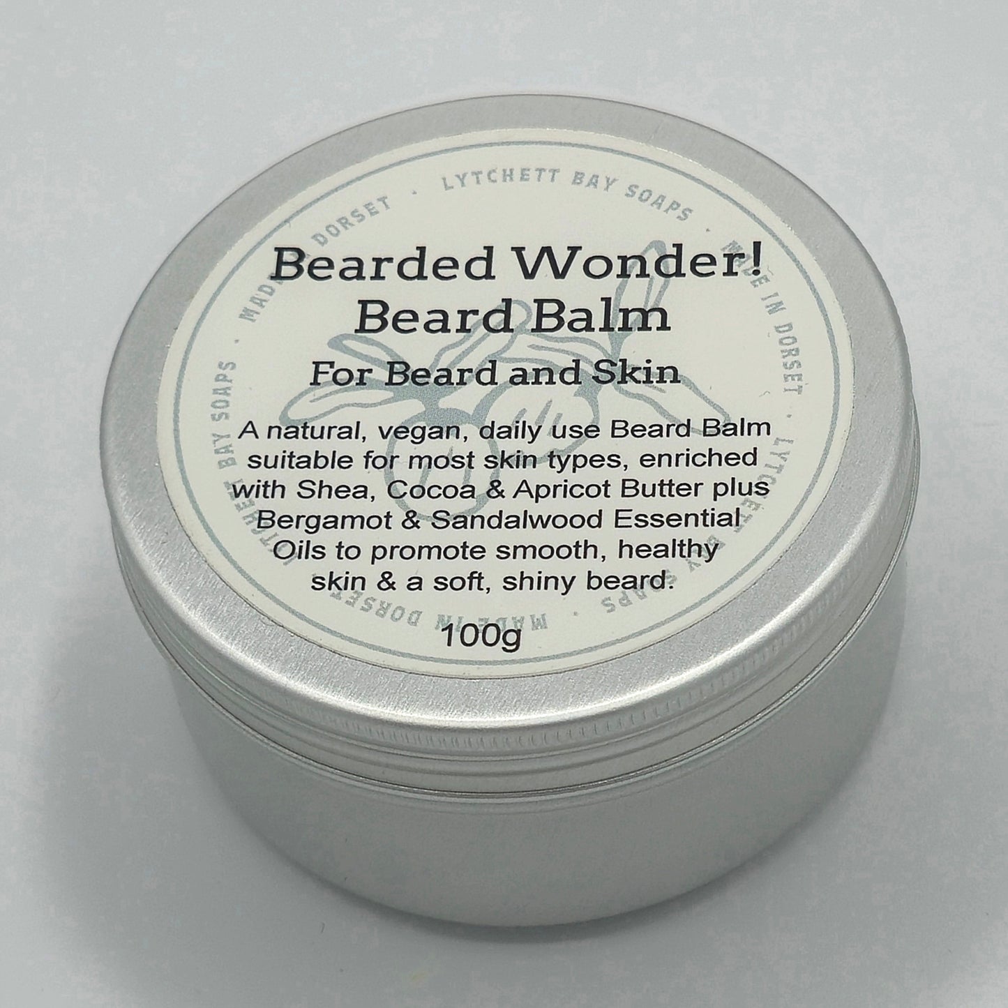 Round silver tin, around 7cm diameter, with light coloured label saying "Bearded Wonder! Beard Balm For Beard and Skin. A natural, vegan, daily use Beard Balm suitable for most skin-types, enriched with Shea, Cocoa & Apricot Butter plus Bergamot & Sandalwood Essential Oils to promote smooth, healthy skin & a soft, shiny beard. 100g".