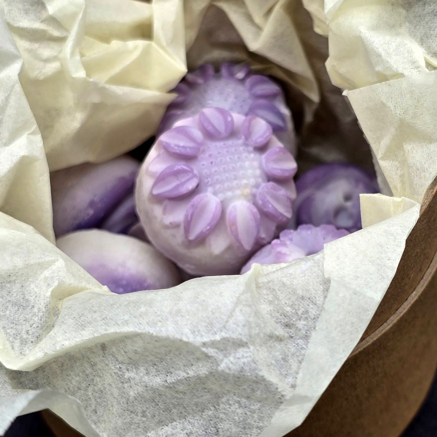Close up of purple flower shaped wax melts inside ivory tissue paper.