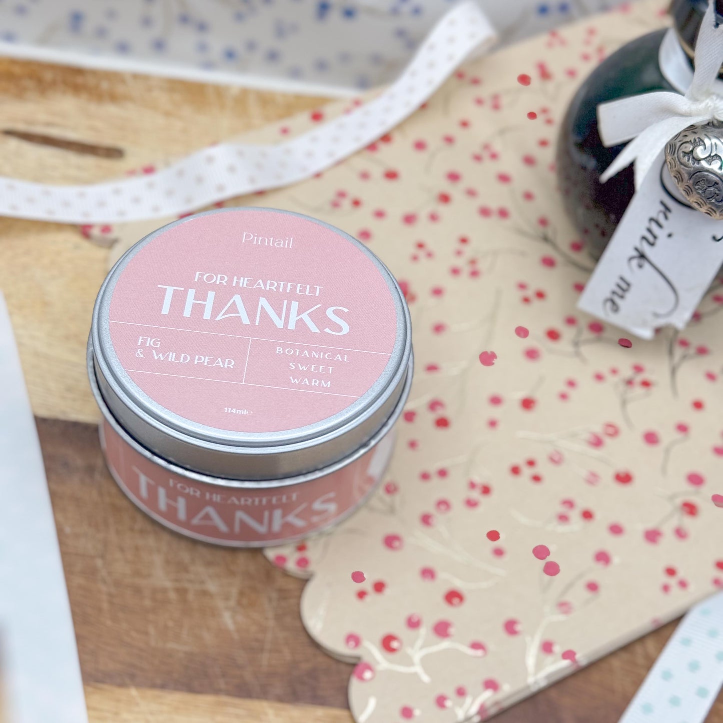 Looking down on the lid of candle tin with a pink label and the wording "For Heartfelt Thanks", "Fig & Wild Pear", "Botanical, Sweet, Warm".