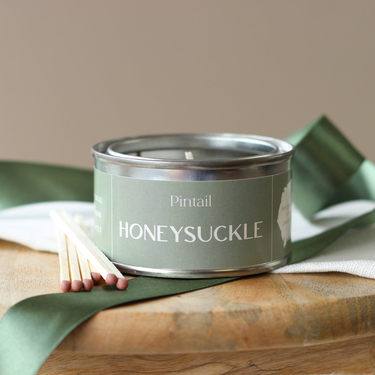 Side view of petite paint pot candle tin from Pintail Candles with a light green label containing the name "Honeysuckle".