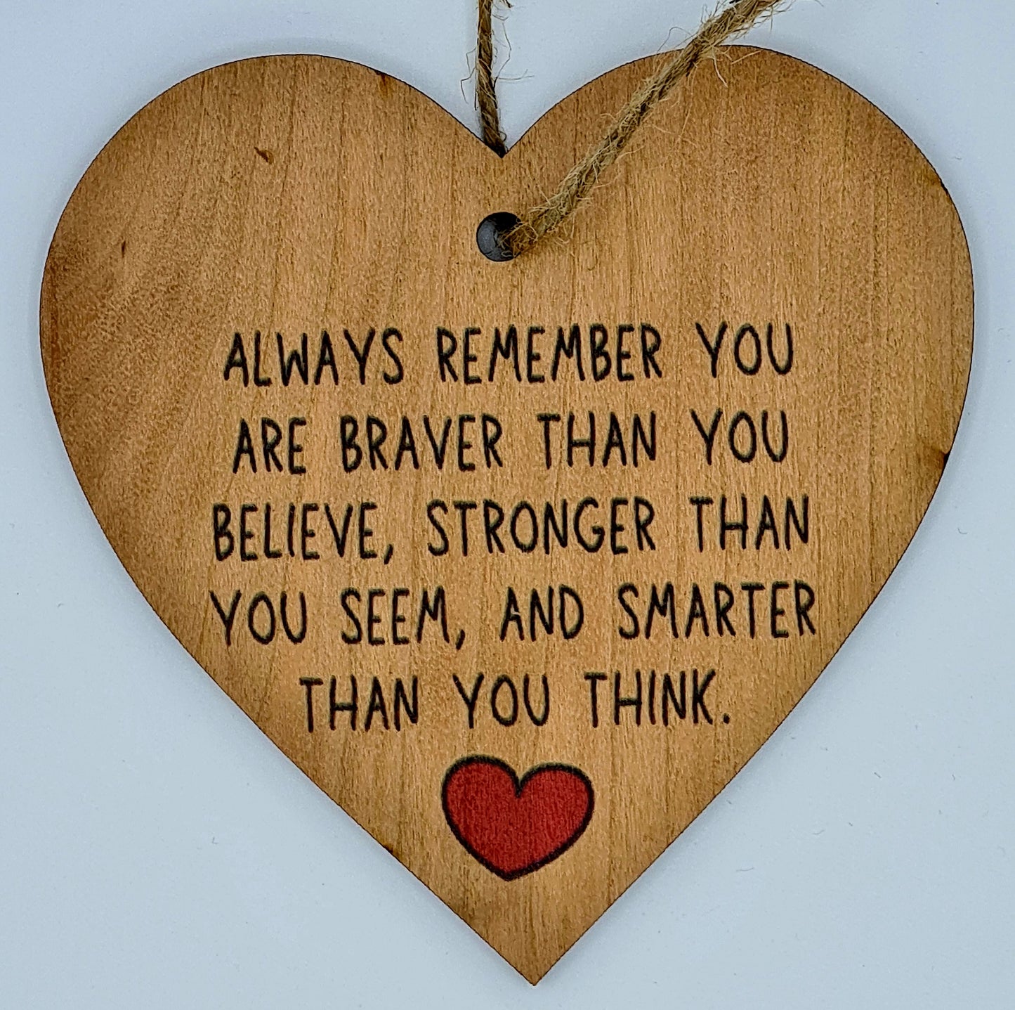 Heart shaped wooden plaque with the slogan "Always Remember you are braver than you believe, stronger than you seem, and smarter than you think". There is a little red heart underneath the writing and a jute string at the top for hanging.