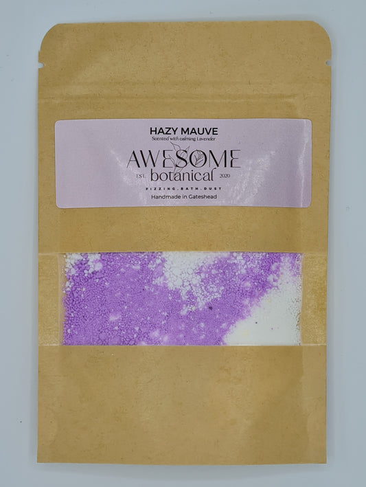 Brown Kraft pouch with lilac label from Awesome Botanical stating Hazy Mauve, scented with calming lavender. There is a small clear window within the pouch showing purple and white coloured bath dust.