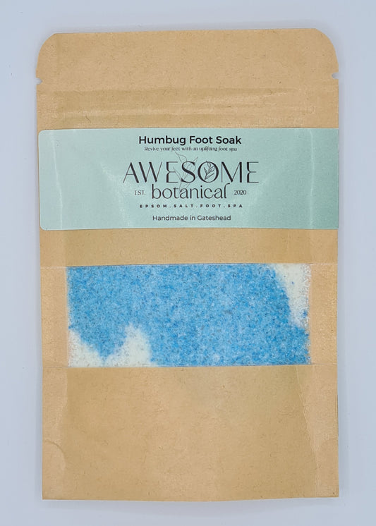 Brown Kraft pouch with light green label from Awesome Botanical stating Humbug Foot Soak, revive your feet with an uplifting foot spa. There is a small clear window within the pouch showing blue and white epsom salts. 