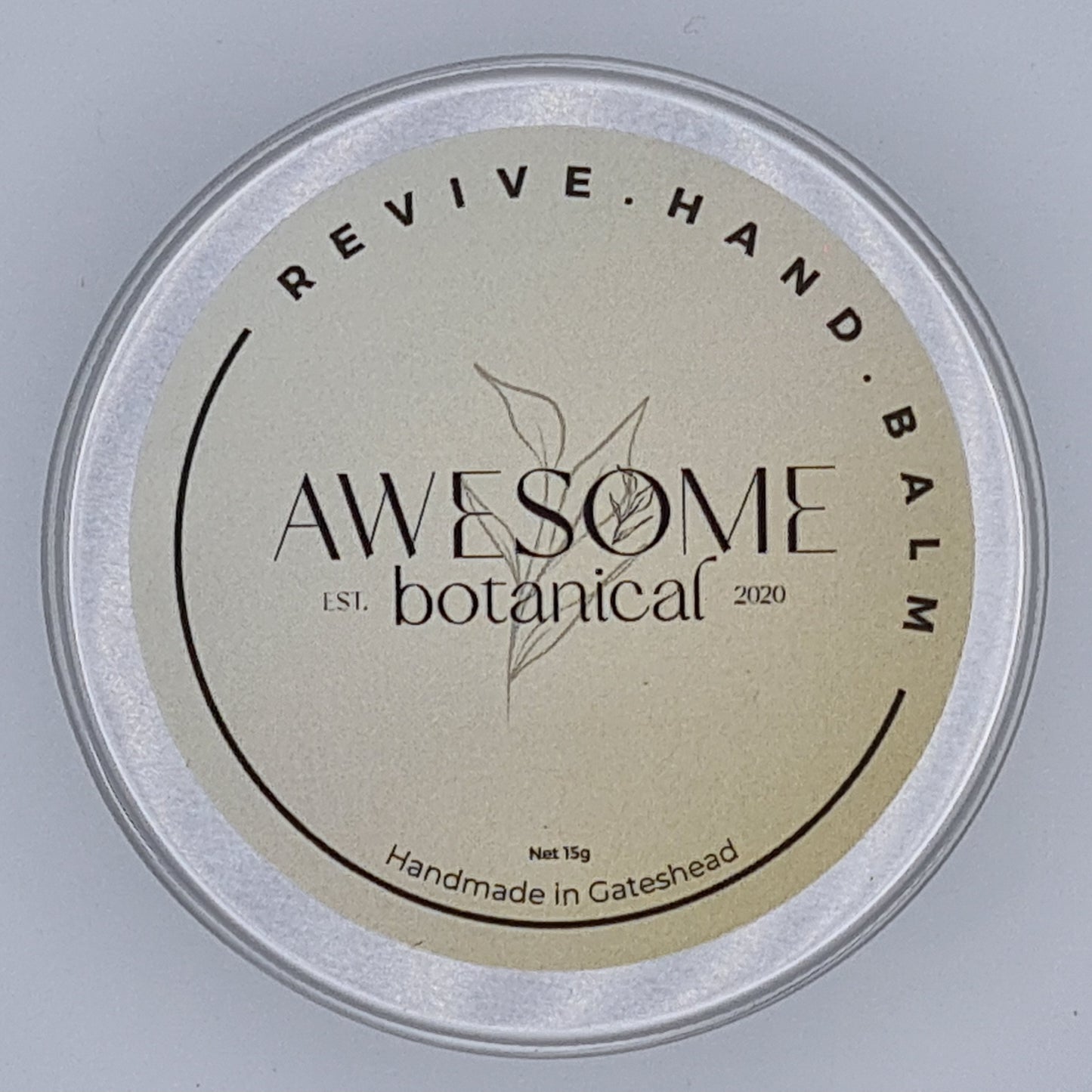 Silver tin with cream label from Awesome Botanical stating Revive Hand Balm.