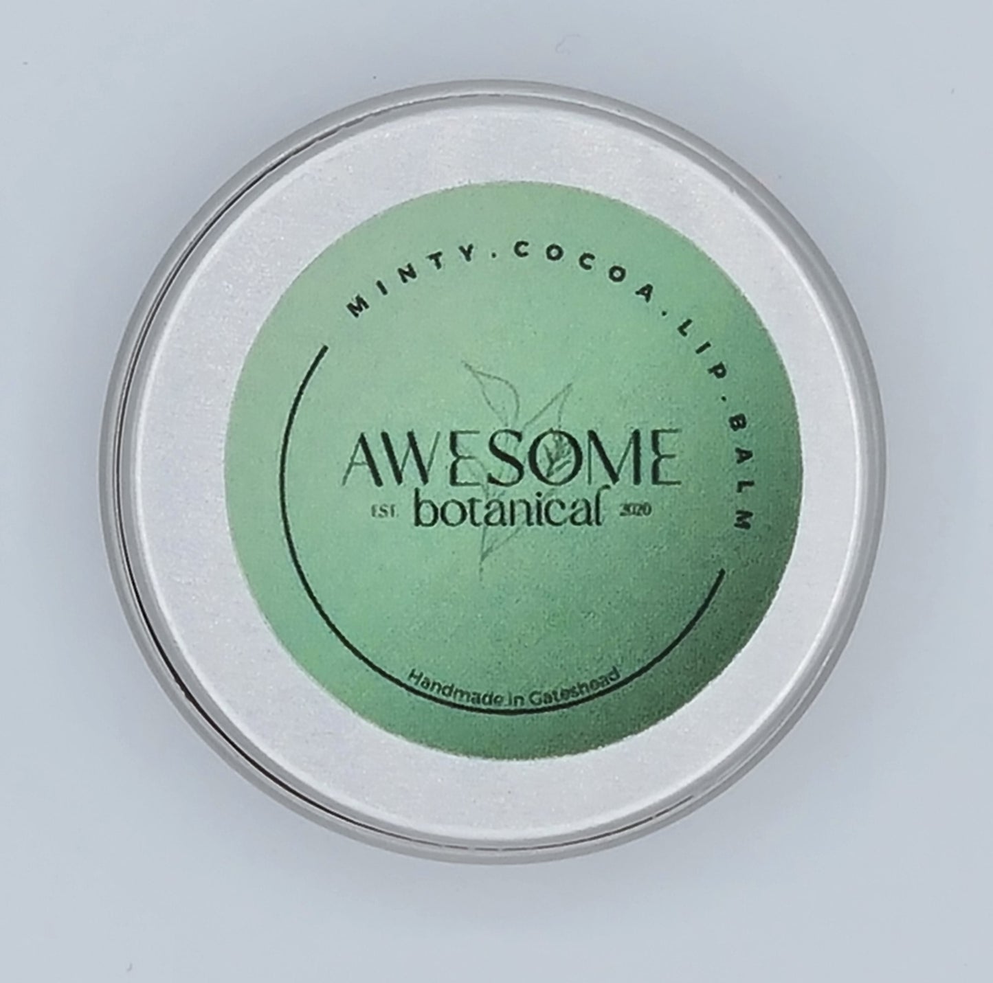 Small silver tin with green label from Awesome Botanical stating Minty Cocoa Lip Balm.