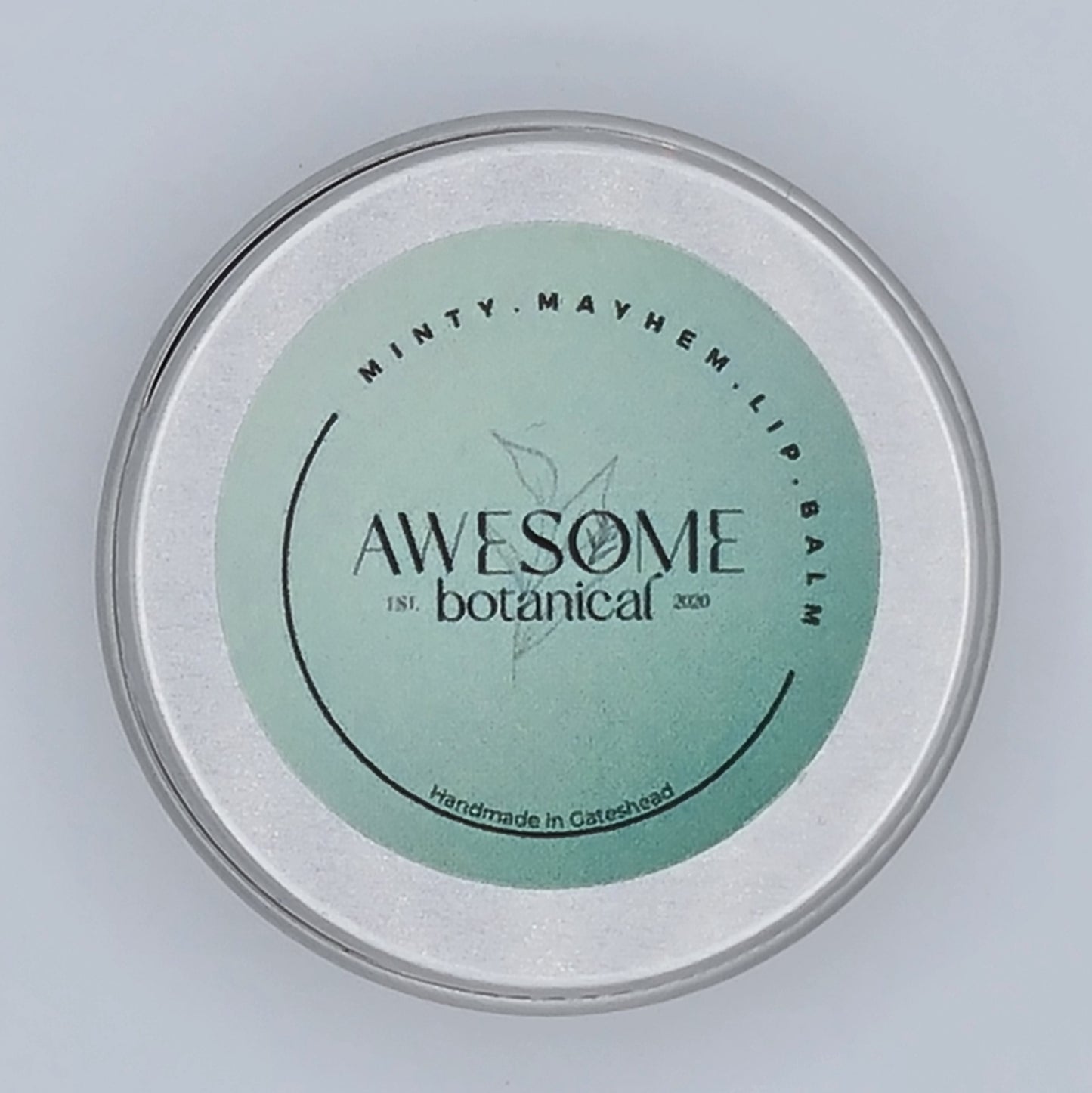 Small silver tin with light green label from Awesome Botanical stating Minty Mayhem Lip Balm.