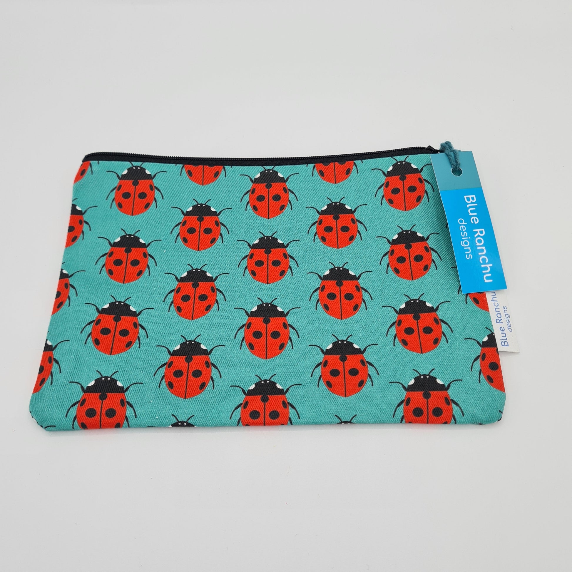 Turquoise cotton accessories bag with print of red and black Ladybirds all over. The bag features a black zip and there is a label attached saying "Blue Ranchu Designs".