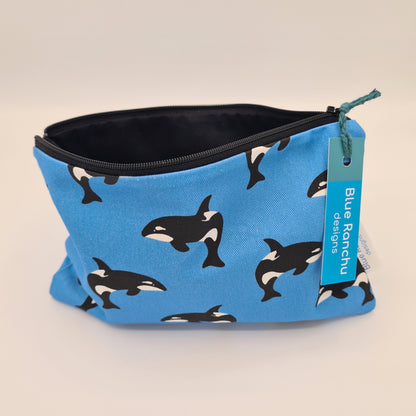 Blue cotton accessories bag with print of black and white Orca whale all over. The bag is open and unzipped showing the black cotton lining inside. There is a label for "Blue Ranchu Designs" attached to the zip.