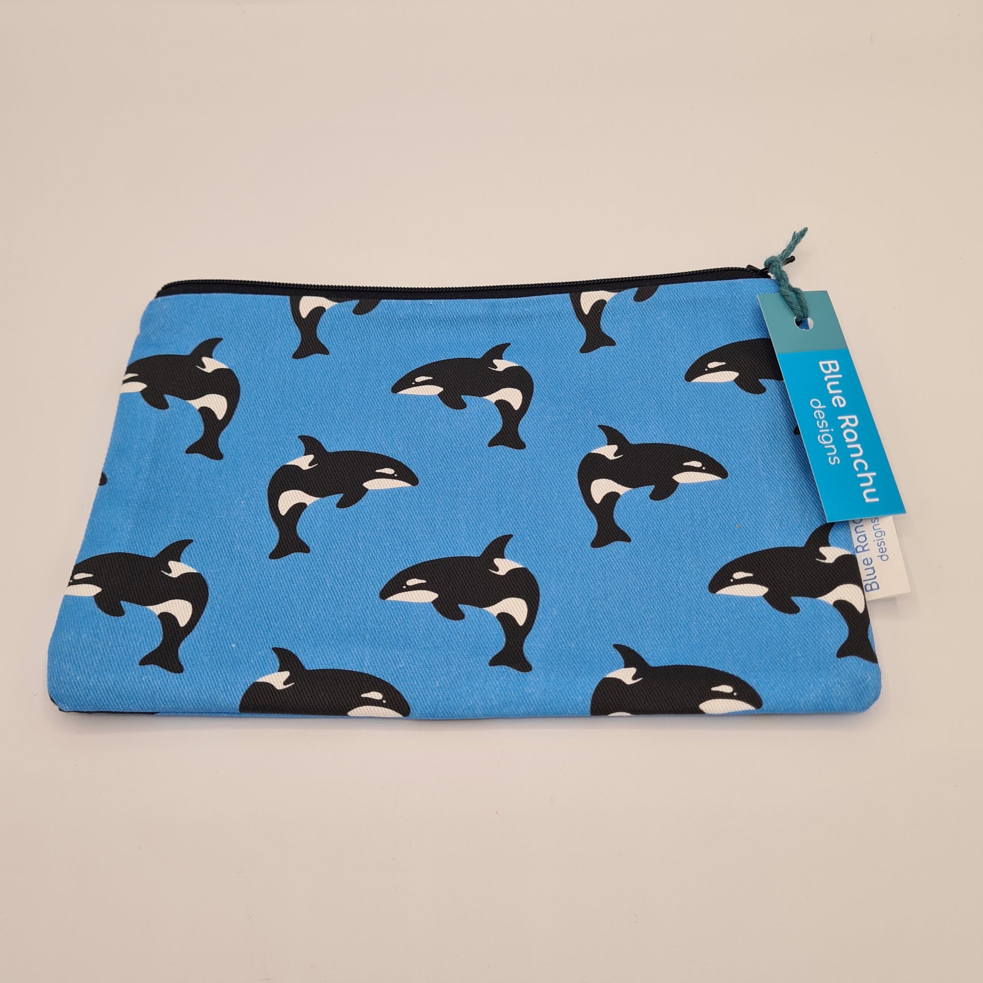 Blue cotton accessories bag with print of black and white Orca whale all over. The bag features a black zip and there is a label attached saying "Blue Ranchu Designs".