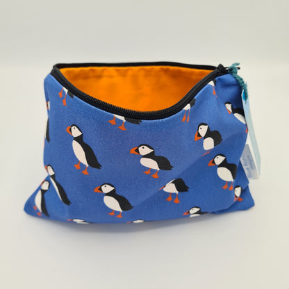 Blue cotton accessories bag with print of black and white Puffins with orange beaks and feet. The bag is open and unzipped showing the bright orange cotton lining inside. There is a label for "Blue Ranchu Designs" attached to the zip.