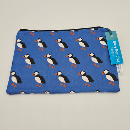 Blue cotton accessories bag with print of black and white Puffins with orange feet and beaks. The bag features a black zip and there is a label attached saying "Blue Ranchu Designs".