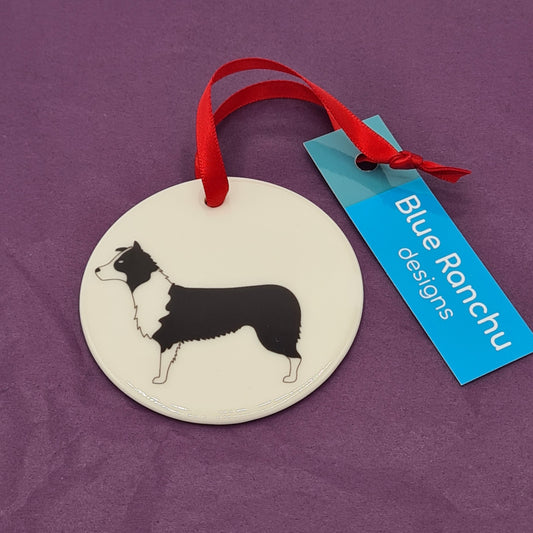 Circular white ceramic hanging decoration featuring a print of a black and white Border Collie There is a red ribbon attached for hanging and a label saying "Blue Ranchu Designs".