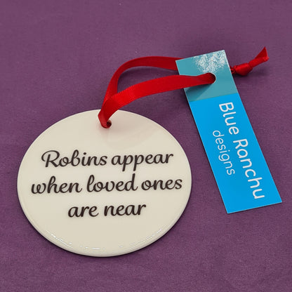 Circular white ceramic hanging decoration featuring the text "Robins appear when loved ones are near". There is a red ribbon attached for hanging and a label saying "Blue Ranchu Designs".