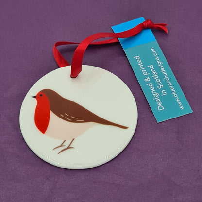 Circular white ceramic hanging decoration featuring a print of a Robin with red breast. There is a red ribbon attached for hanging and a label saying "Designed & printed in Scotland" and the website address for Blue Ranchu Designs.