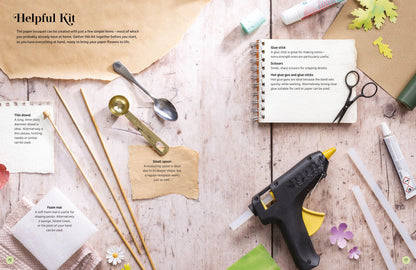A styled flat-lay of a DIY craft kit labeled 'Helpful Kit' on a light wood background, featuring a hot glue gun, glue sticks, scissors, wooden sticks, small spoons, paper pieces, and printed instruction cards.