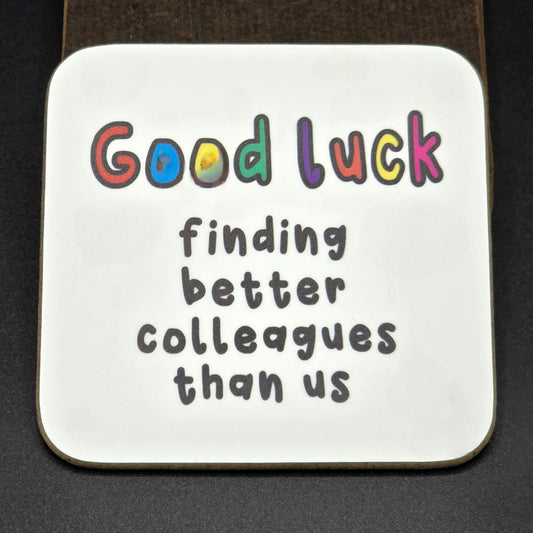 White coaster with the wording "Good Luck finding better colleagues than us".