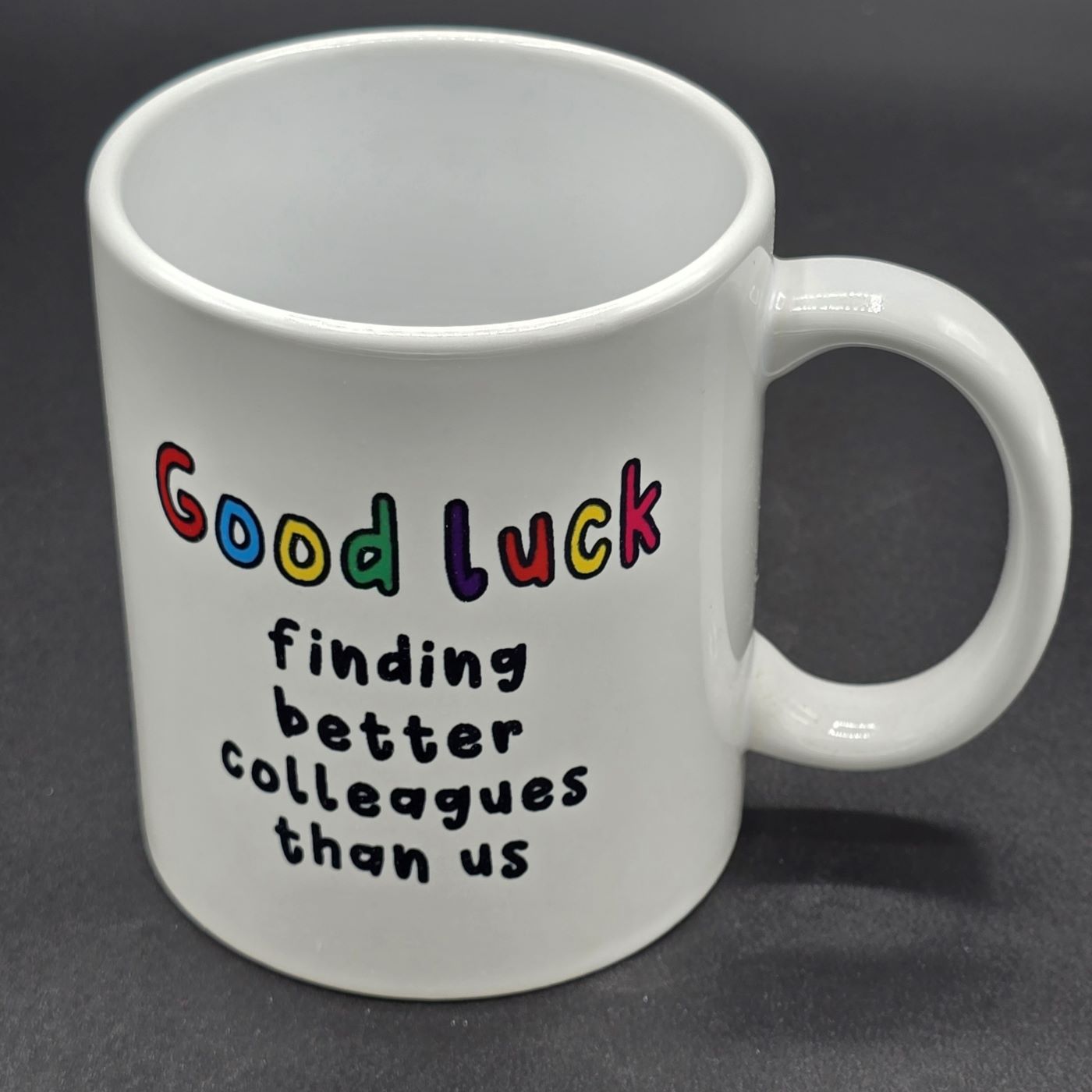 White mug with handle. Text on the mug says" Good Luck finding better colleagues than us".