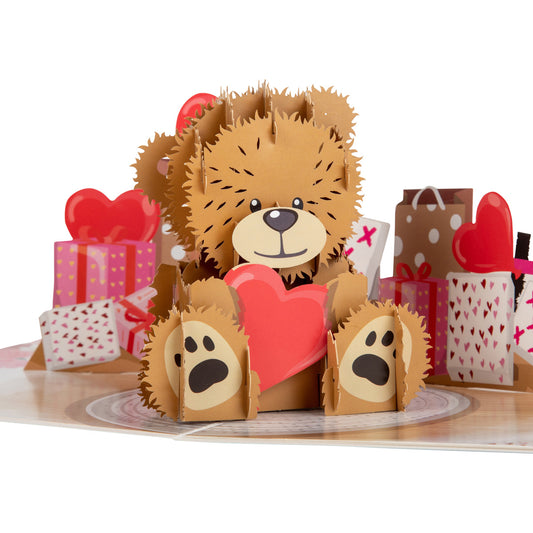 Close up of Love Bear pop up card showing a cute brown teddy bear holding a red love heart. The bear is surrounded by a selection of wrapped gifts.