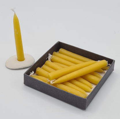 The inside of the small square box showing 11 mini yellow beeswax candles. The 12th candle is standing in the mini ceramic holder next to the box.