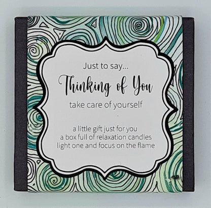 Small black square box with a blue and green swirly label with white text box saying "Just to say...Thinking of You, take care of yourself. A little gift just for you, a box full of relaxation candles, light one and focus on the flame". 