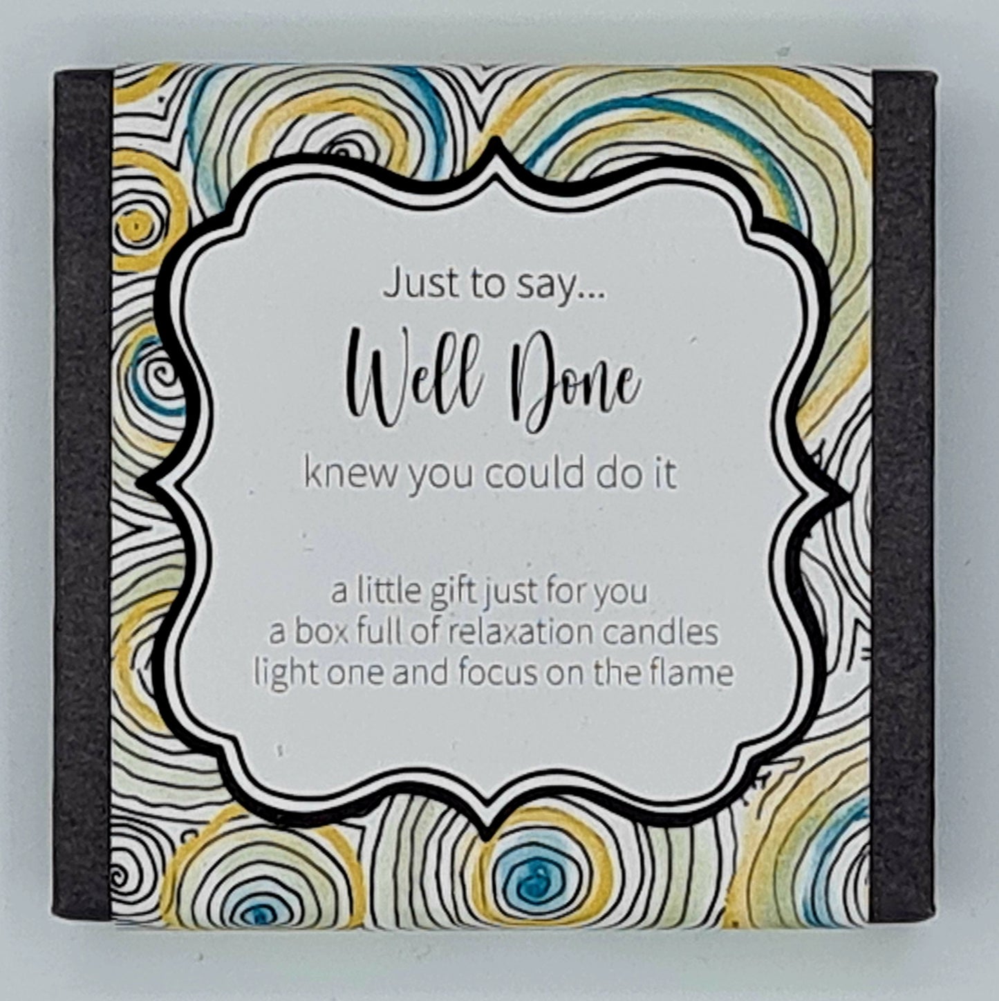 Small black square box with a yellow and blue swirly label with white text box saying "Just to say...Well Done, knew you could do it. A little gift just for you, a box full of relaxation candles, light one and focus on the flame".