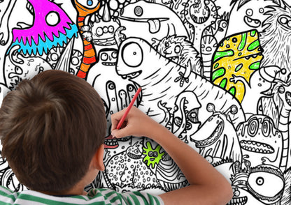 Aerial image showing a young boy colouring in the Monsters Giant Colouring Poster. He is holding a red pencil and some of the monsters have been coloured in in various colours.