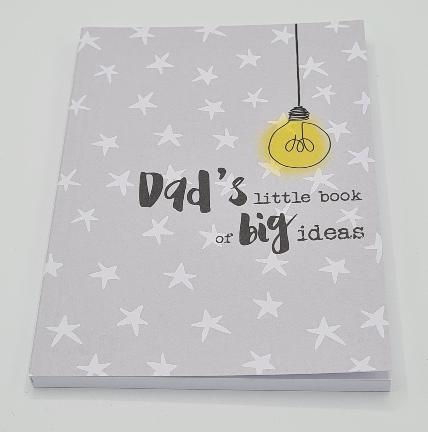 A6 notebook with a grey front cover covered with white stars and featuring a drawer of a yellow light bulb with the wording "Dad's little book of big ideas".