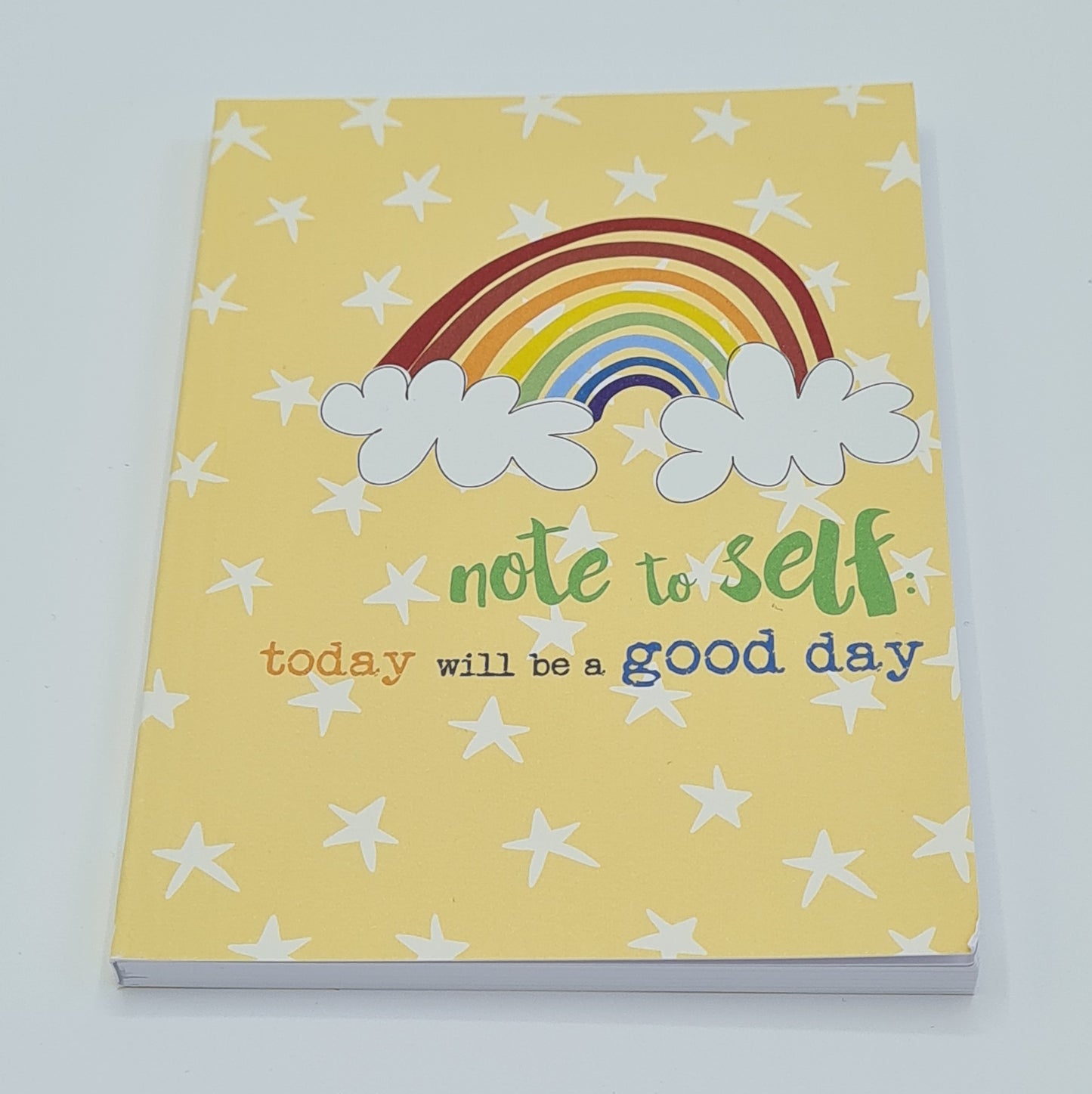 A6 notebook with a yellow front cover with white stars all over it. There is a drawing of a rainbow with text below saying "Note to self: today will be a good day".