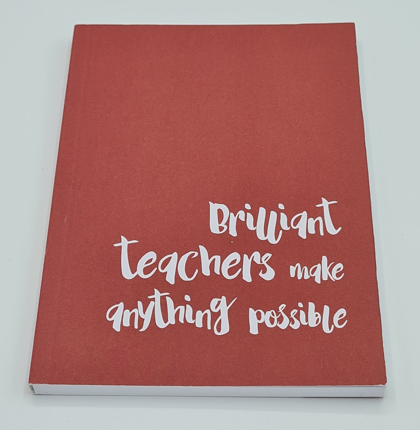 Image shows A6 notebook with red front cover. White text reads "Brilliant teachers make anything possible".