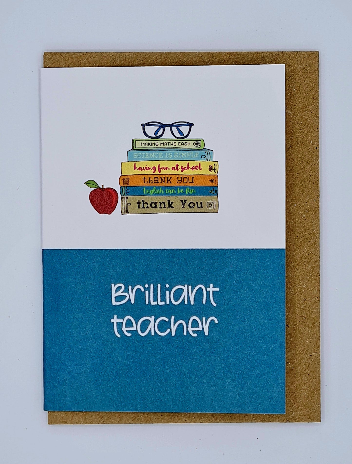 A7 mini card with brown envelope behind. The card is blue at the bottom with the words "Brilliant Teacher". The top half of the card is white with a drawing of a red apple next to pile of books topped by a pair of glasses.