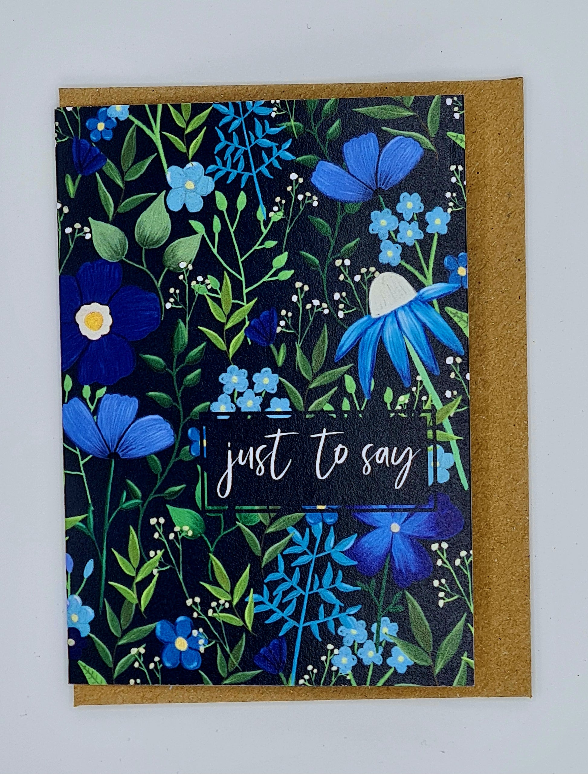 A7 mini card with brown envelope. The card is dark coloured with lots of flowers in varying shades of blue with lots of leaves and greenery and features a rectangular box with the words "Just to say" written in white