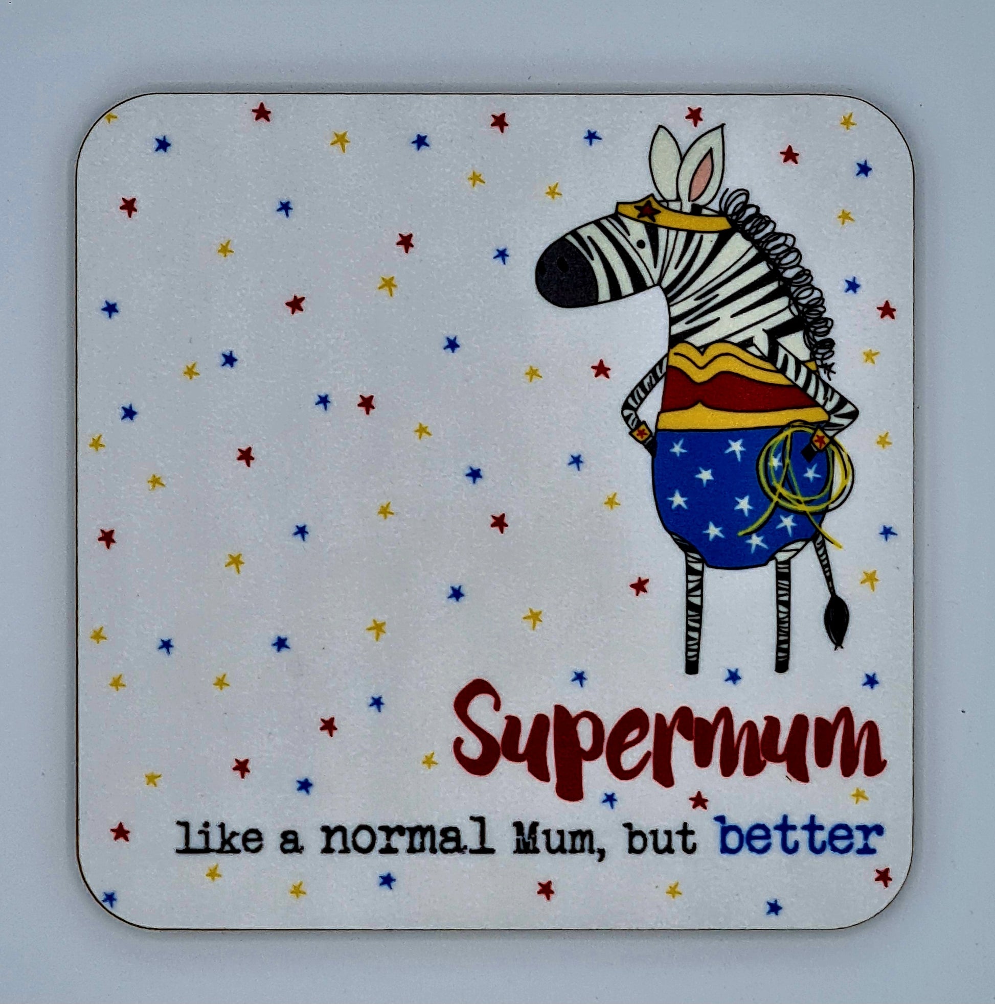 White coaster covered with red, yellow and blue stars. There is a drawing of a zebra dressed as wonder woman and the slogan reads "Supermum, like a normal mum, but better". 